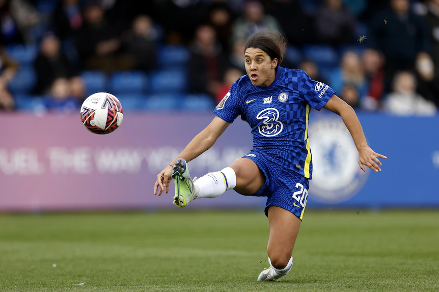 A soccer player wearing blue stretches out her leg to kick the ball