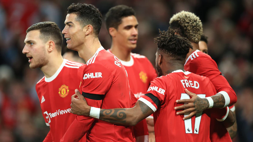 A group of Manchester United male players embrace as they celebrate a Premier League goal.